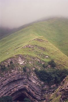 a large green hill covered in lots of grass next to a small tunnel on top of a mountain