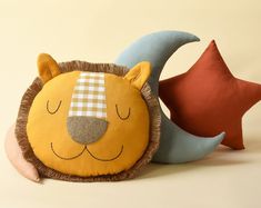 a lion pillow with a sleeping face on top of it next to a star shaped pillow