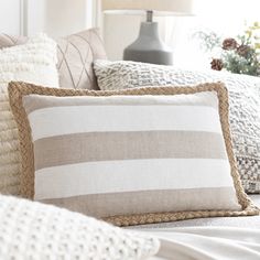 the pillows on the bed are striped in beiges and white, while the pillow is made from jute