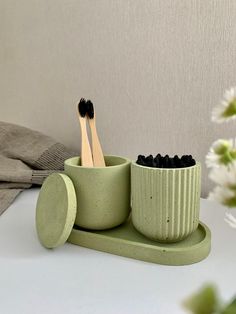 two toothbrushes are in a green cup on a table next to a flower