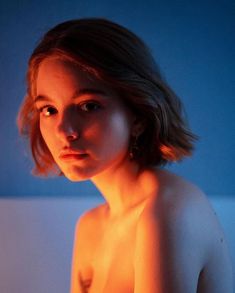 a naked woman with no shirt on in front of a blue wall and lit by a candle