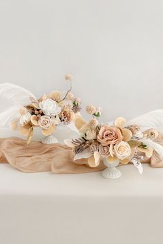 an arrangement of flowers and angel wings on a white tableclothed surface with neutral colors