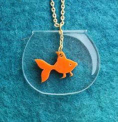 an orange fish in a glass bowl on a gold plated chain necklace that is sitting on a blue carpet