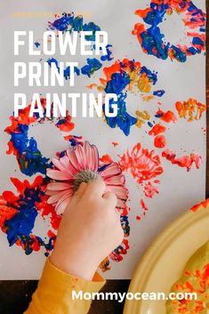 a child's hand holding a flower in front of an art project with flowers painted on it