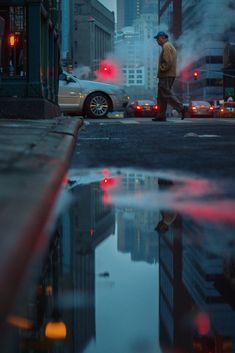 a man walking across a street next to a puddle filled with water and traffic lights