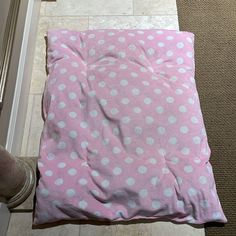 a pink and white polka dot blanket laying on the floor next to a person's feet