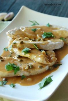 a white plate topped with meat covered in gravy and garnished with parsley