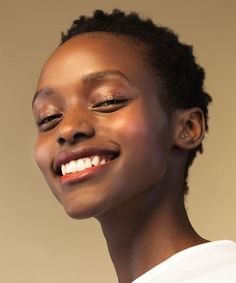 a woman smiling with her eyes closed while wearing a white t - shirt and gold earrings