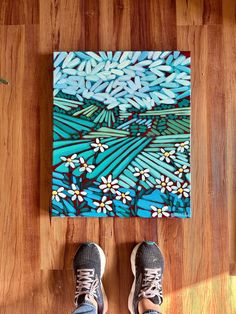 a person standing in front of a painting on a wooden floor with their feet up