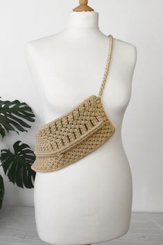 a white mannequin with a beige woven purse on it's back and a green plant in the background