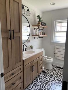 a bathroom with black and white tile flooring, wooden cabinets and a round mirror