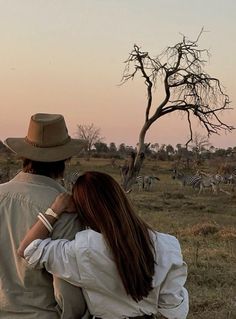 a man and woman sitting on the back of a horse watching zebras in the distance