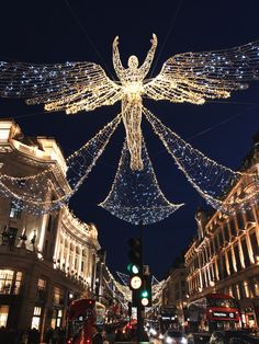 an angel statue is lit up in the middle of a busy city street at night