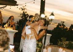 two women hugging each other in front of people at an outdoor dinner table with candles