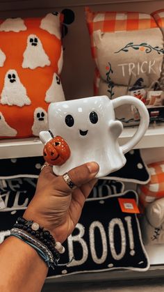 a hand holding a coffee mug with a smiling face on it in front of halloween pillows