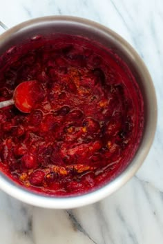 a bowl filled with red liquid on top of a marble countertop next to a spoon