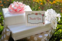 a thank you card sitting on top of two gift boxes in the middle of some grass