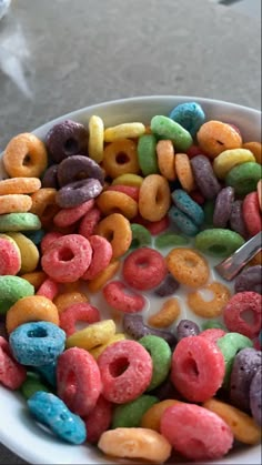 a bowl filled with lots of different colored donuts next to a cup of milk