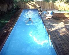 two people are swimming in a pool surrounded by wooden decking and fenced area