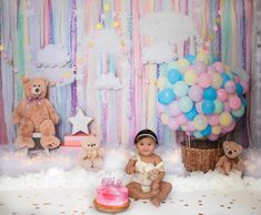 a baby sitting in front of a cake and balloons