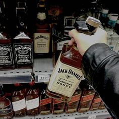 a person is holding a bottle of jack daniels in front of bottles of alcohol on the shelf