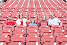 three adults and two children sitting in red stadium seats with their hands up to the sky