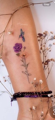 a woman's tattoo with flowers and butterflies on her side, next to dried grass