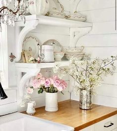 a white kitchen with pink flowers in vases on the counter and shelves above it