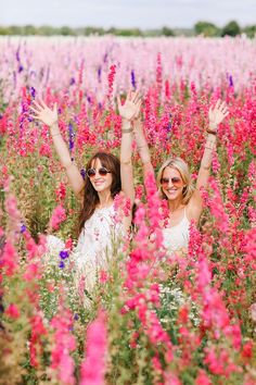 two women standing in a field full of flowers with their hands up and arms outstretched