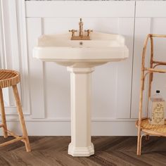 a white pedestal sink sitting on top of a wooden floor next to two stools