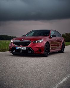 a red car is parked on the side of the road in front of dark clouds