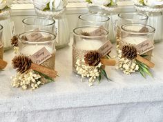 several glass jars with pine cones and flowers in them are sitting on a white table cloth