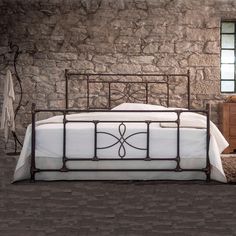 a bedroom with stone walls and flooring has a metal bed frame in the middle