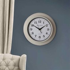 a white clock hanging on the side of a blue wall next to a beige chair