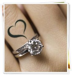 a woman's engagement ring with a heart tattoo on her left hand and a diamond in the middle