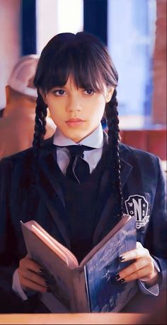 a girl with braids is holding a book in her hands and looking at the camera