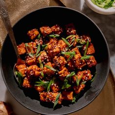 a black bowl filled with tofu and greens