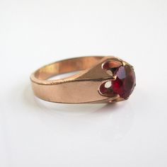 a gold ring with a red stone in the center on a white surface, it appears to be worn