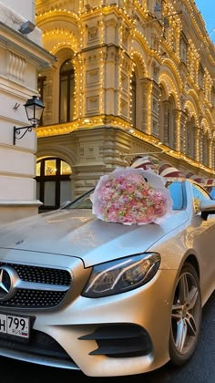 a silver car parked in front of a building with flowers on the hood and windows