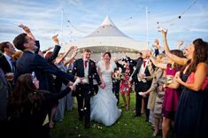 a bride and groom walk through confetti thrown by their guests in front of a marquee