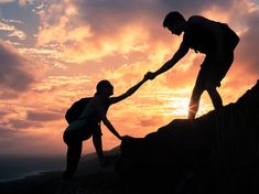 two people are helping each other to climb up a mountain at sunset or sunrise with the sun setting behind them