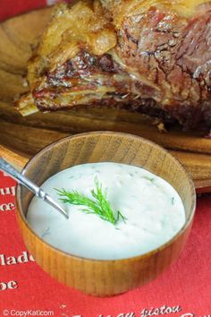 a wooden plate topped with meat next to a bowl of yogurt