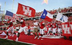 the football team is running onto the field with flags in their hands and onlookers watching