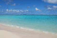 an empty beach with clear blue water and clouds