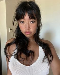 a woman with long black hair wearing a white tank top and posing for the camera