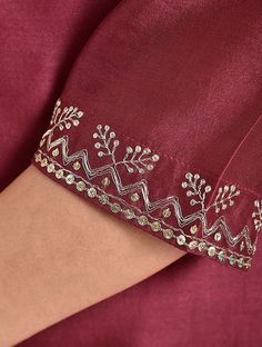 a woman's arm wearing a maroon dress with white embroidery on the sleeves and cuffs