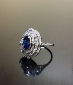 DeKara Designs Collection Art Deco Inspired Extremely Elegant Halo Sapphire Diamond Engagement Ring. Metal- 90% Platinum, 10% Iridium. Stones- 1 Oval Ceylon Blue Sapphire 1.25 Carats, 100 Round Diamonds F-G Color VS2 Clarity .80 Carats. Size- 6 1/4. An Amazing Art Deco Inspired Ceylon Blue Sapphire Triple Halo Diamond Engagement. The ring features a beautiful Ceylon Blue Sapphire that is expertly bezel set in the center. The sapphire is surrounded by 92 pave and burnish set round sparkling diamo Luxury Oval Diamond Cut Sapphire Ring, Formal Sapphire Diamond Cut Ring, Formal Sapphire-colored Diamond Ring, Timeless Marquise Sterling Silver Ring, Round Polished Wedding Jewelry, Round Diamond Ring For Wedding, Round Polished Finish Jewelry For Wedding, Art Deco White Gold Halo Ring, White Gold Art Deco Halo Ring