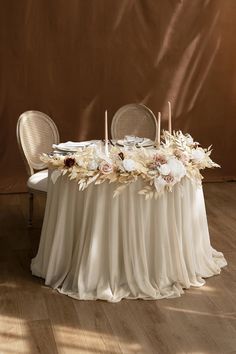 the table is set with white flowers and candles on it, along with two chairs