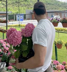 a man holding a potted plant in front of a fenced area with flowers