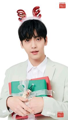 a man in a white suit holding a green box with a red bow on it's head